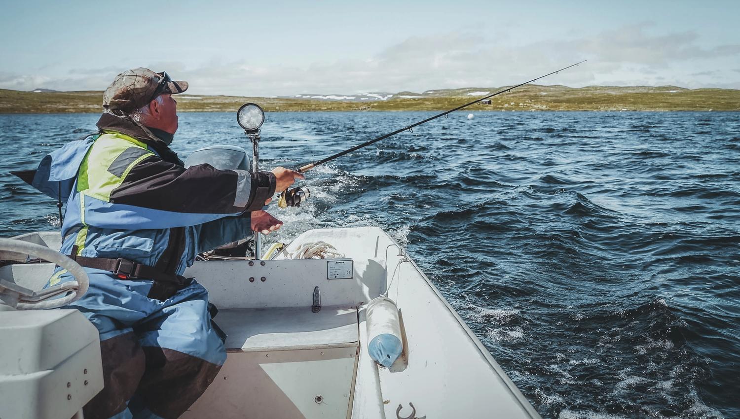 A man is fishing from a boat at the Halnefjord lake in the Hardangervidda.
