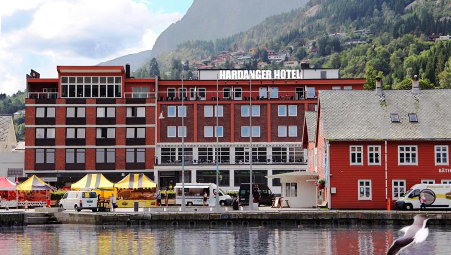 Hardanger Hotel ved fjorden med lokale marknadstelt og majestetiske fjell rundt.
