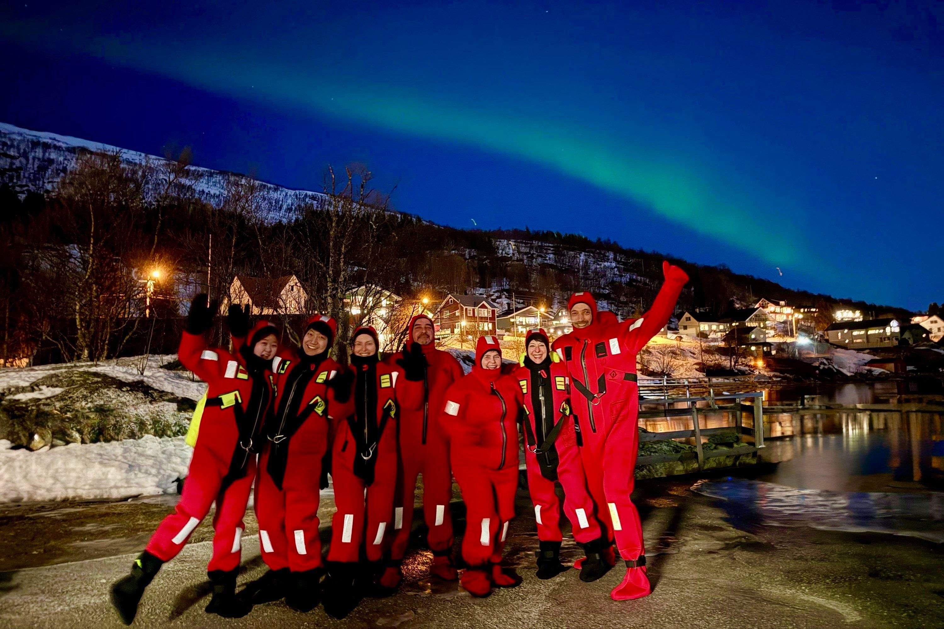 Flere gjester som står under nordlyset i tørrdrakter