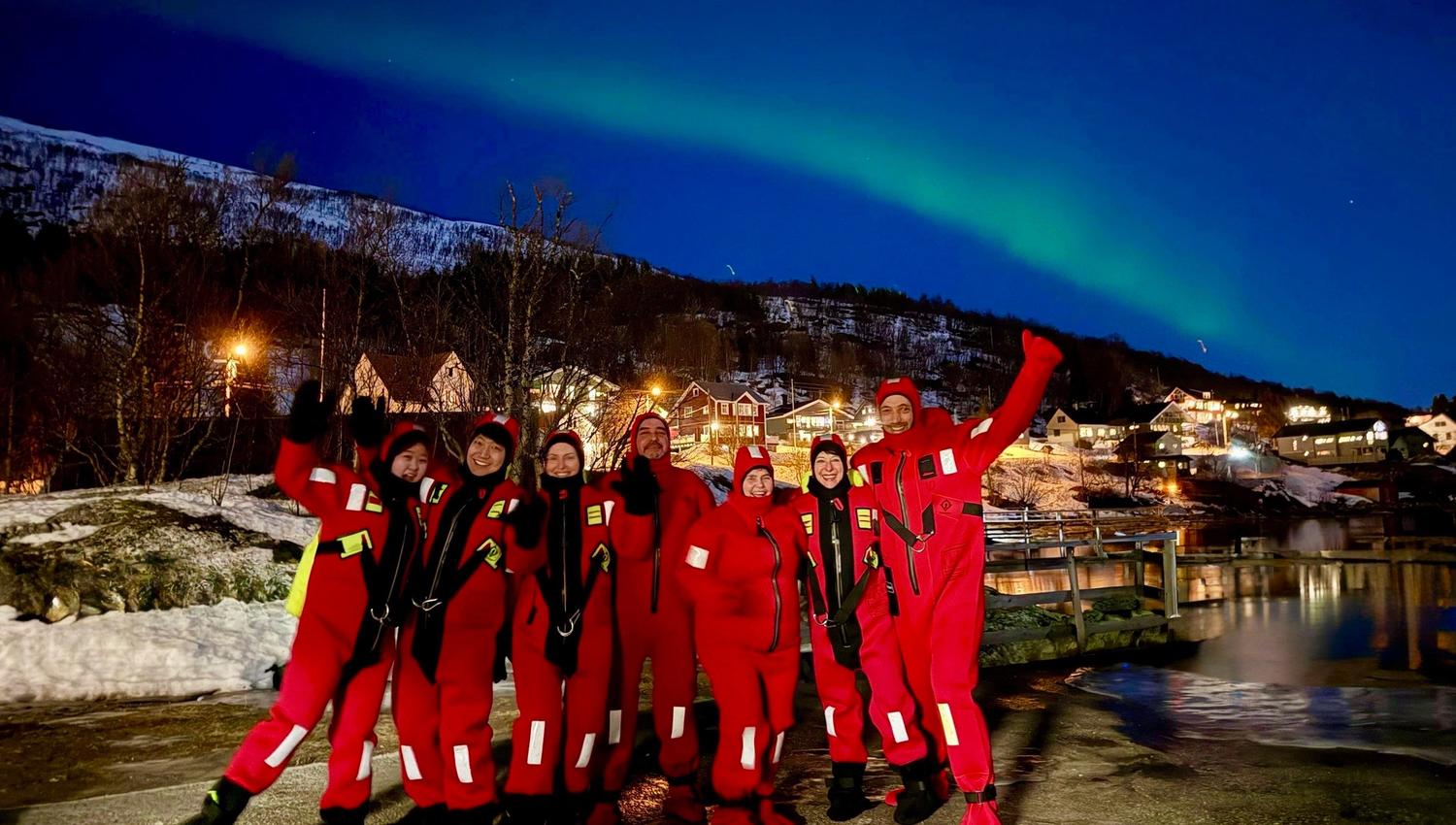 Flere gjester som står under nordlyset i tørrdrakter