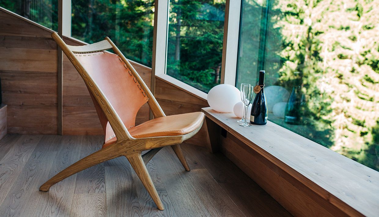 Komfortabelt sitteområde i Woodnest tretopphytte med store vindauge og utsikt til naturen utanfor.