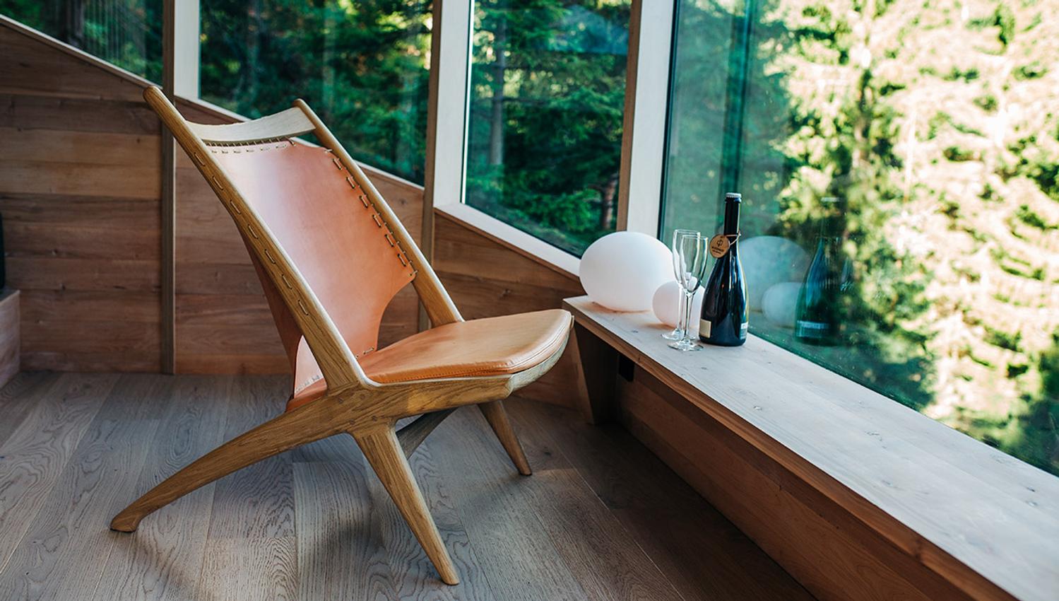 Komfortabelt sitteområde i Woodnest tretopphytte med store vindauge og utsikt til naturen utanfor.
