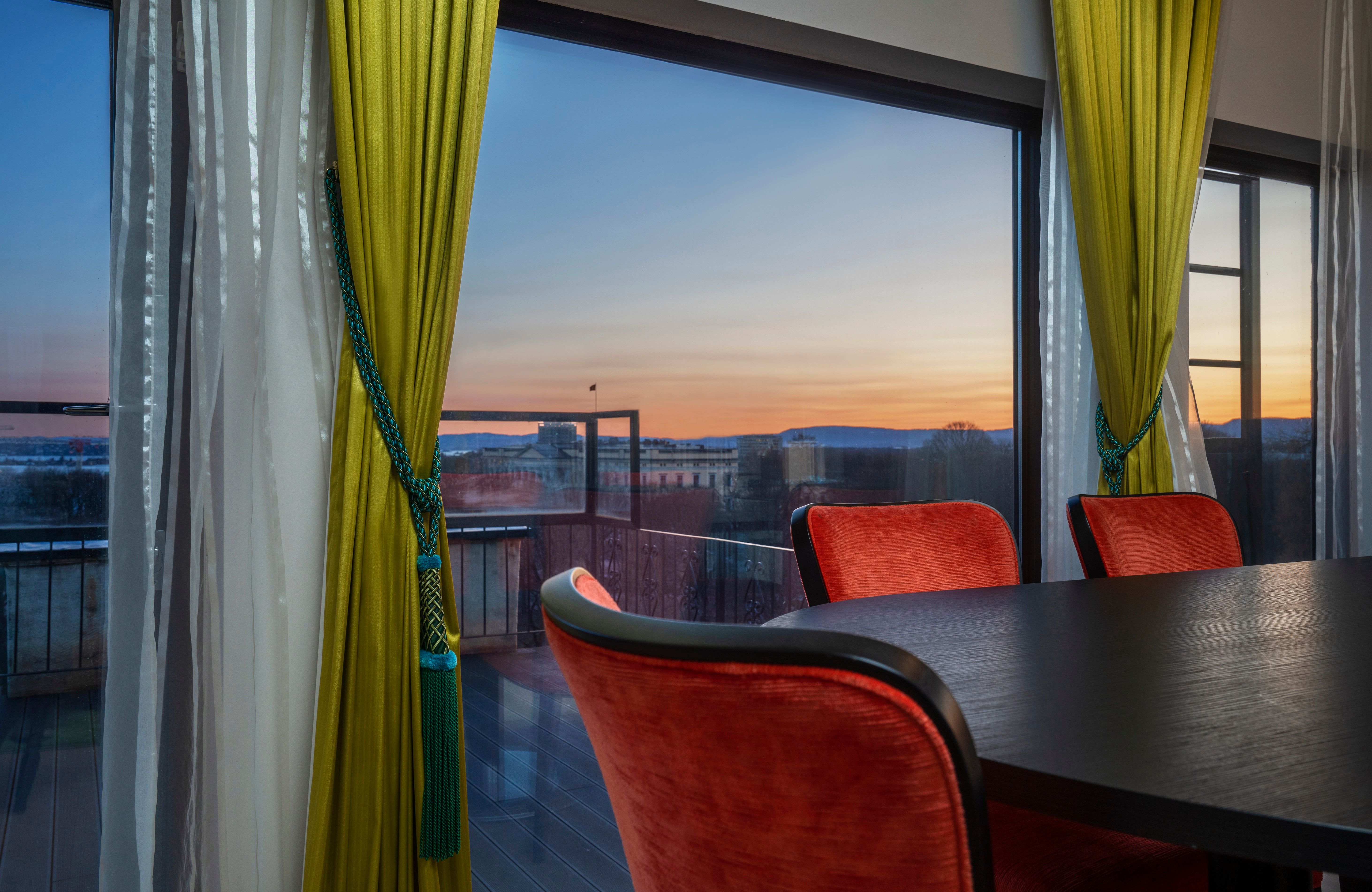 møterom med mørkt bord, røde stoler foran panoramavindu med kveldsutsikt. Thon Hotel Slottsparken, Oslo. Foto