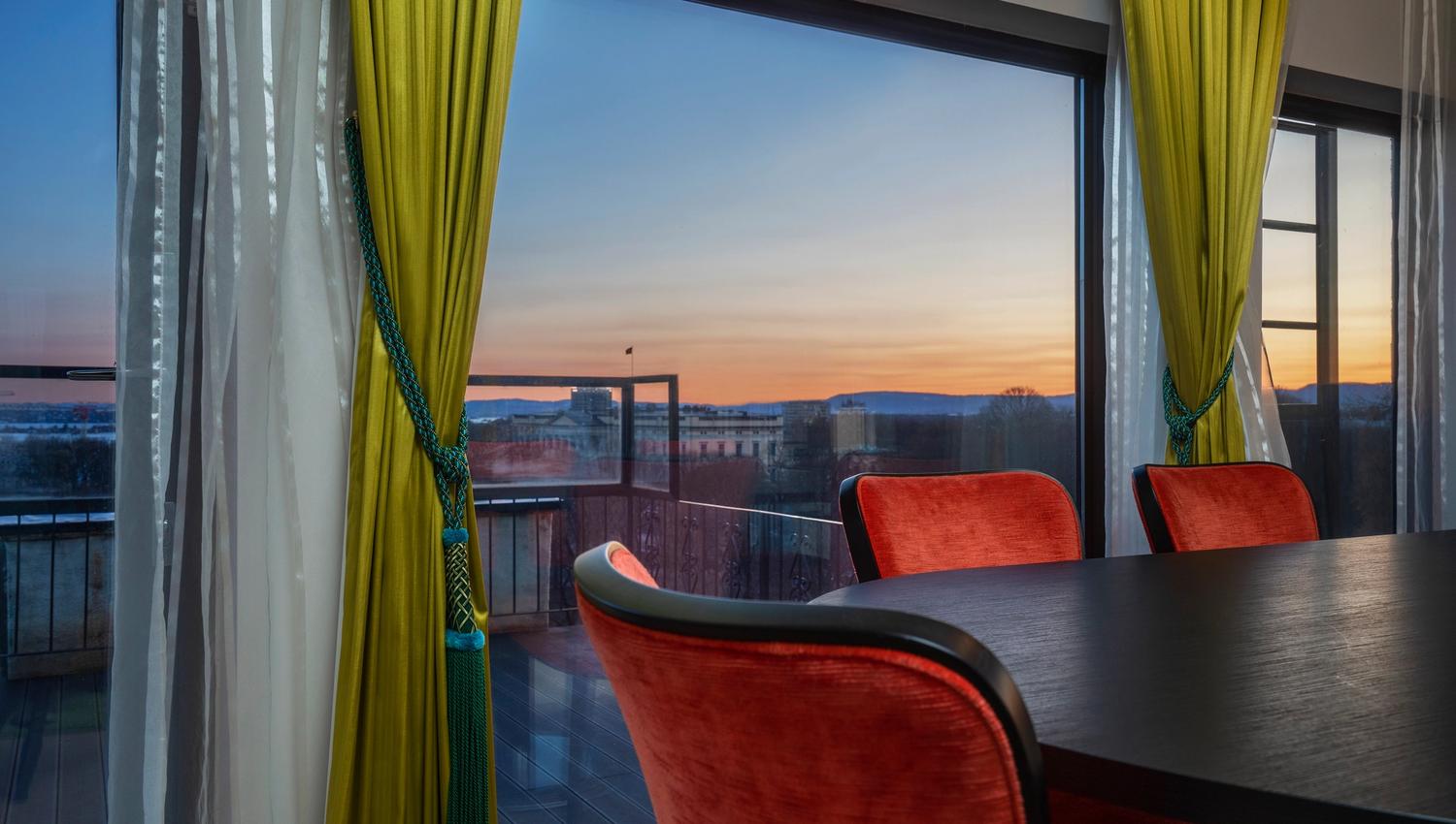 møterom med mørkt bord, røde stoler foran panoramavindu med kveldsutsikt. Thon Hotel Slottsparken, Oslo. Foto
