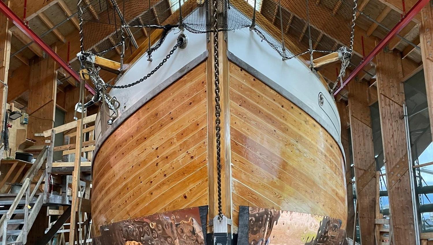 A large wooden boat under restoration inside the workshop building at Hardanger Maritime Center.