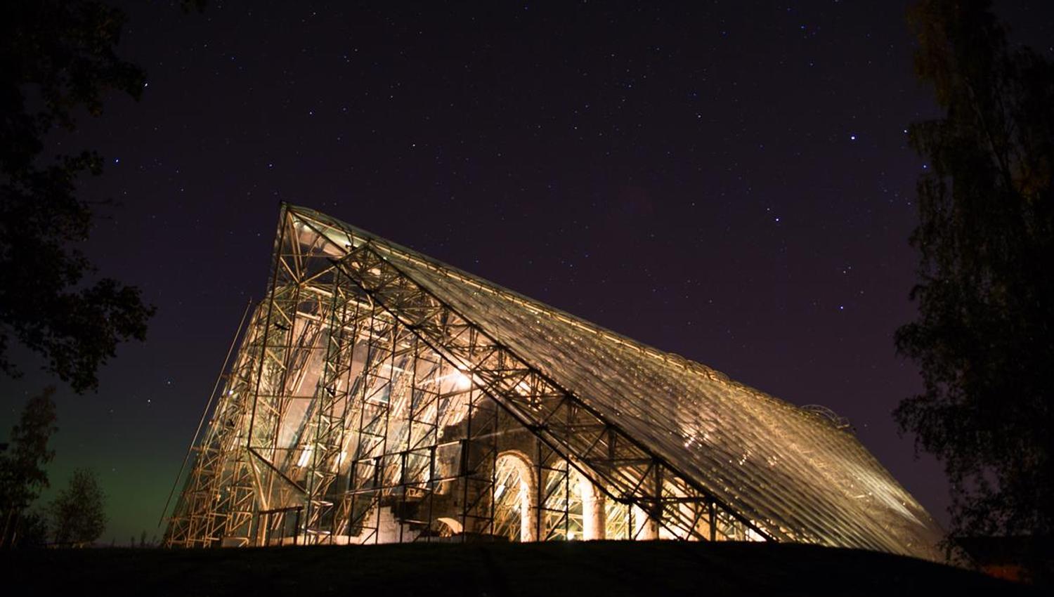 Trestruktur eller paviljong lyser opp i mørket med stjernehimmel over.
