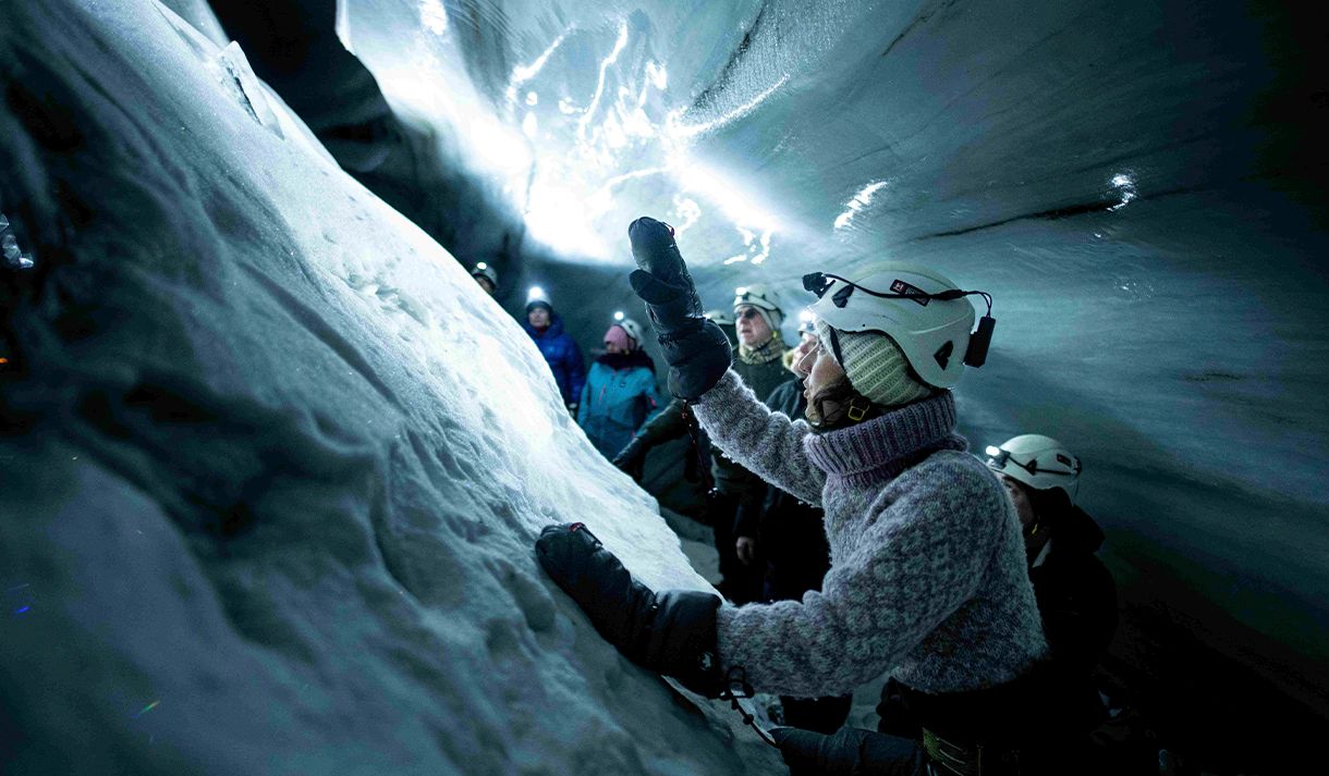 A guide with a headlamp and helmet in the foreground telling guests in the background about the ice cave they're in