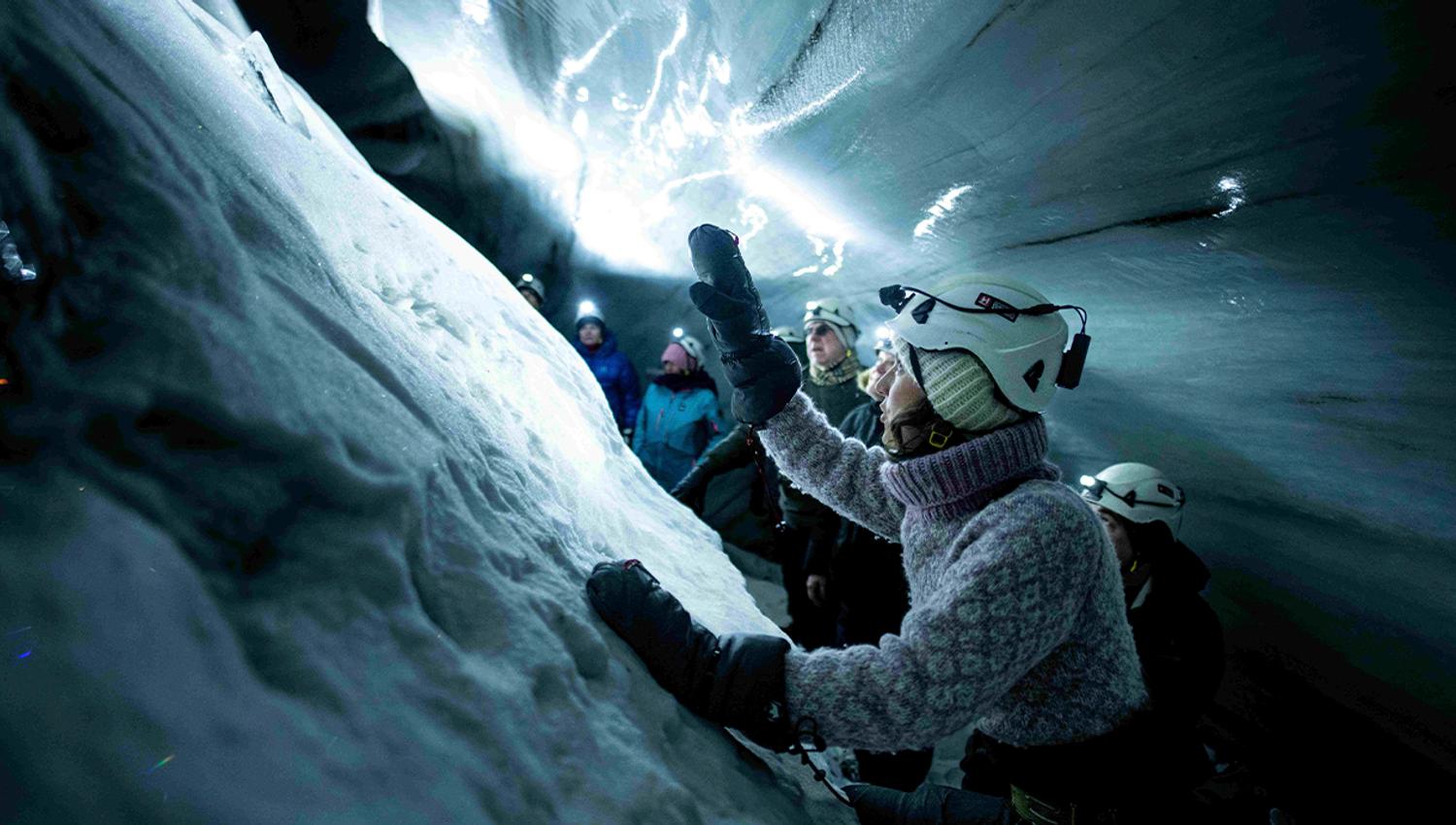 A guide with a headlamp and helmet in the foreground telling guests in the background about the ice cave they're in