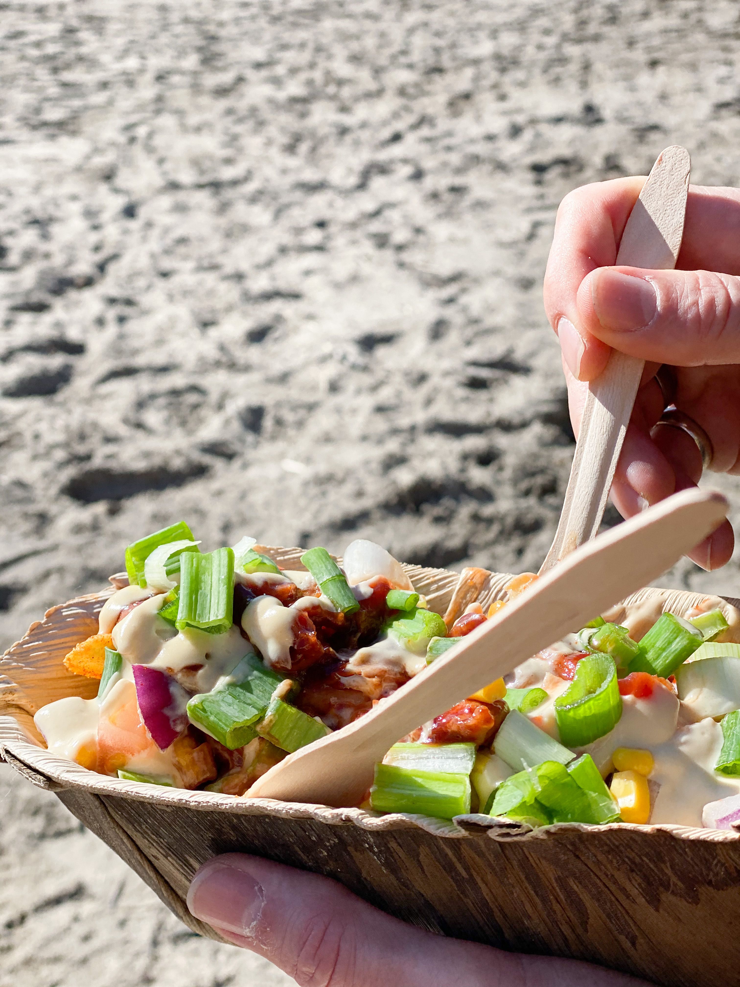 En hånd som holder i en tallerken loaded fries . Sandstrand i bakgrunnen. Foto.