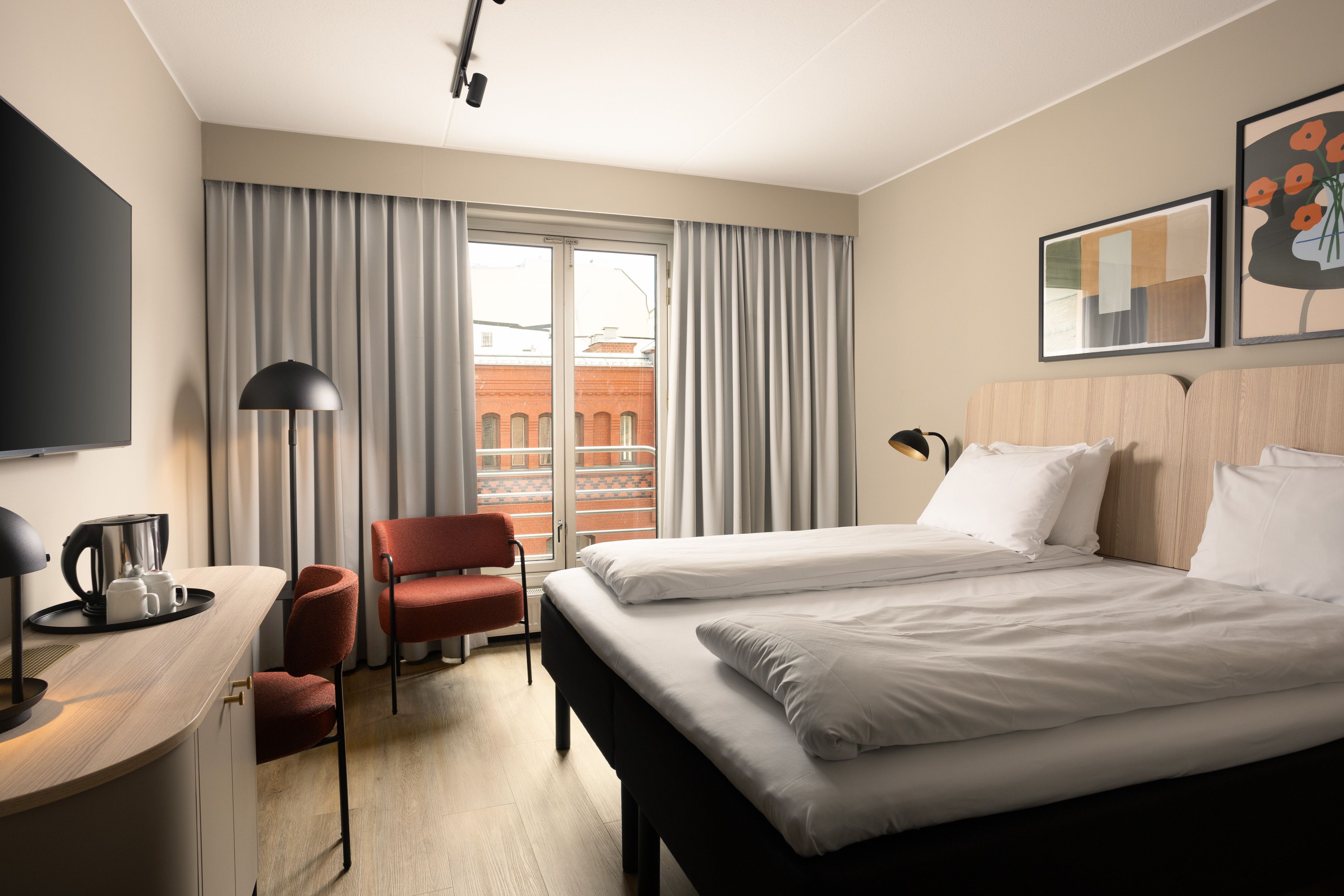 Hotel room with large double bed, TV on the wall, red chair in the corner and grey curtains