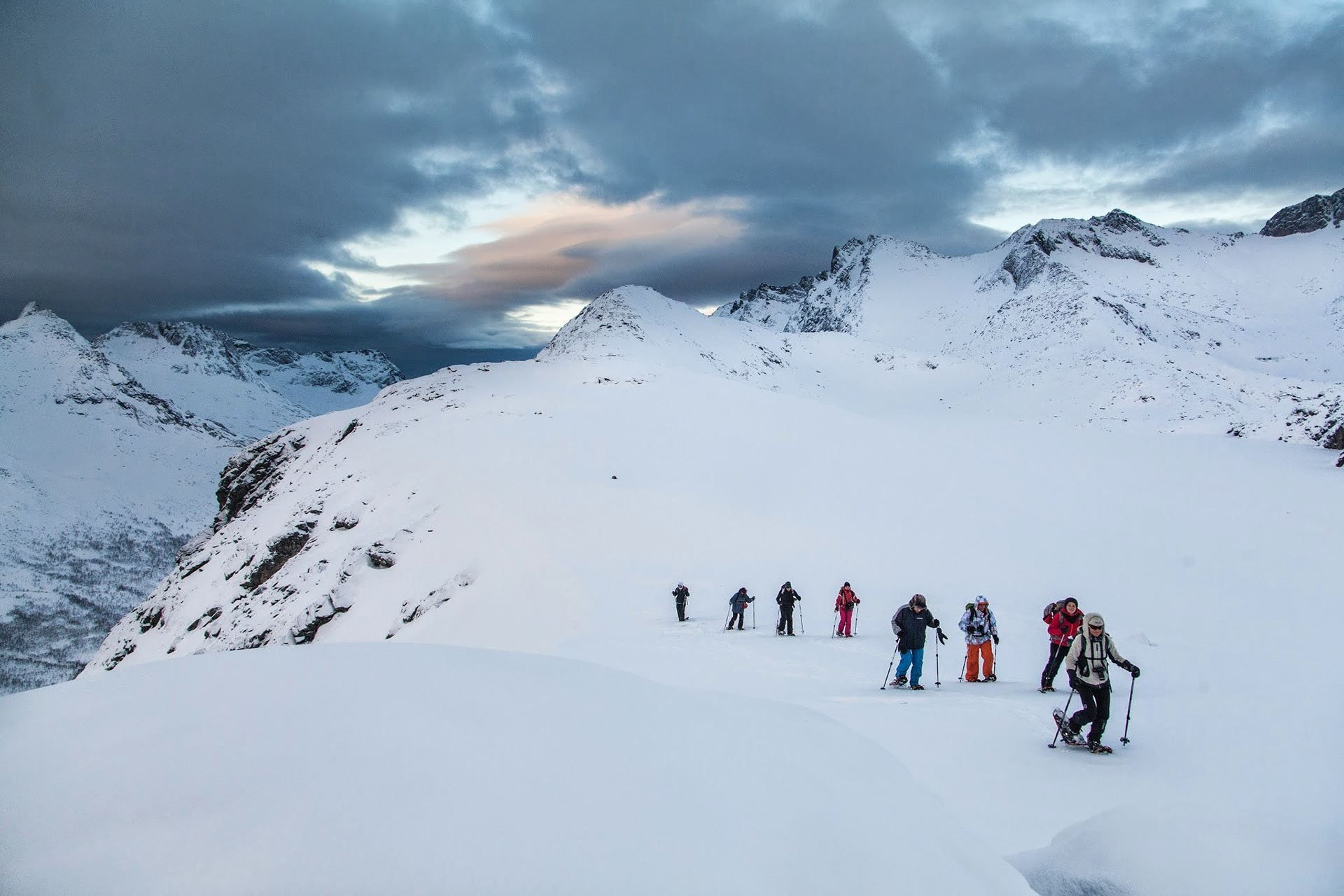 People hiking in snow-covered mountains under a partly cloudy sky.