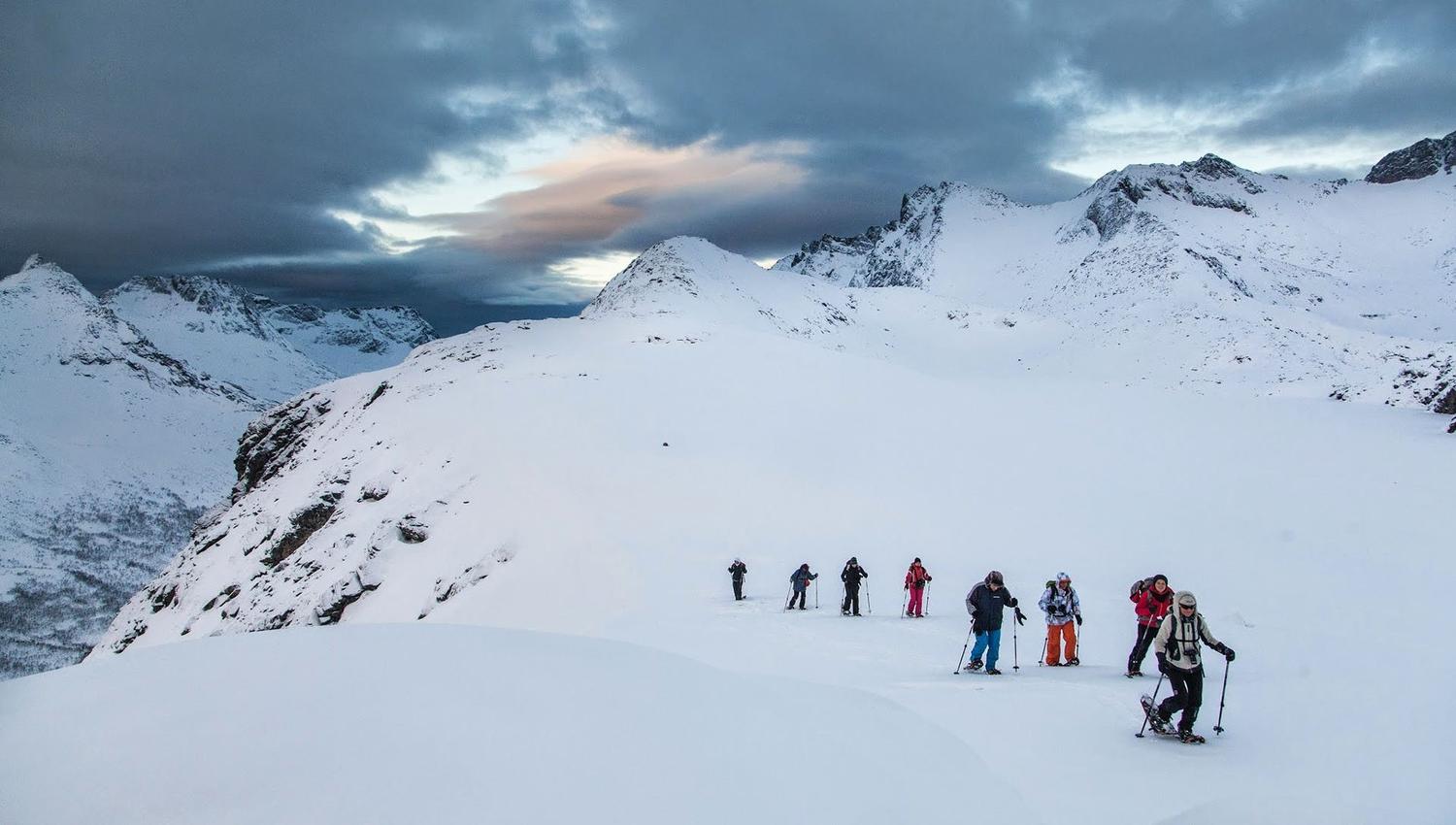 People hiking in snow-covered mountains under a partly cloudy sky.