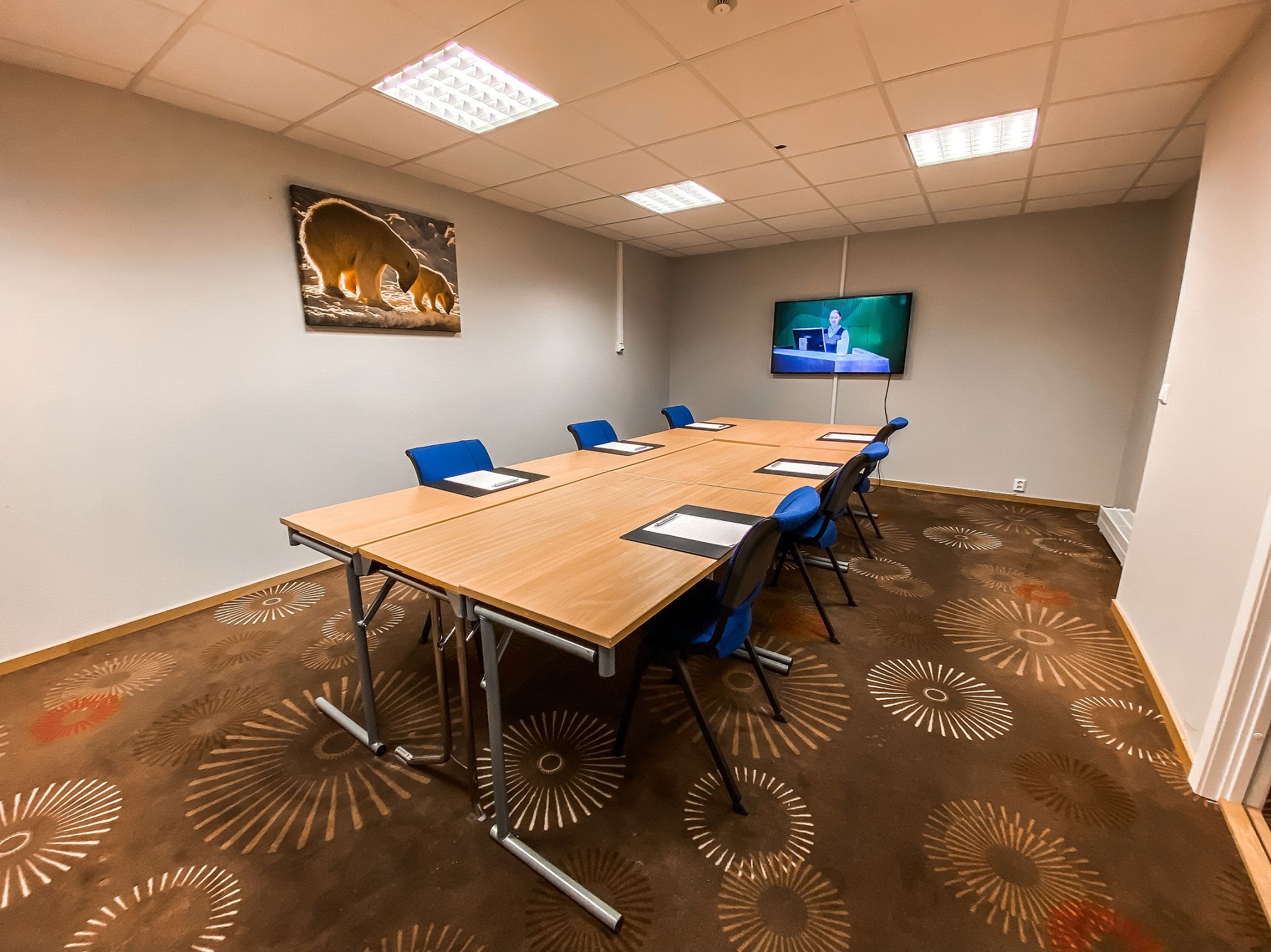 A small conference room with tables, chairs and a screen in the end of the room