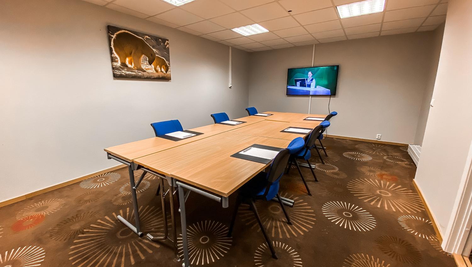 A small conference room with tables, chairs and a screen in the end of the room
