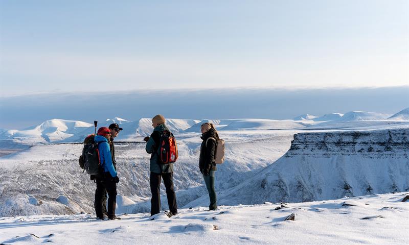 several people standing on top of snowcovered mountain. overlooking plateaus and other mountains in the background 