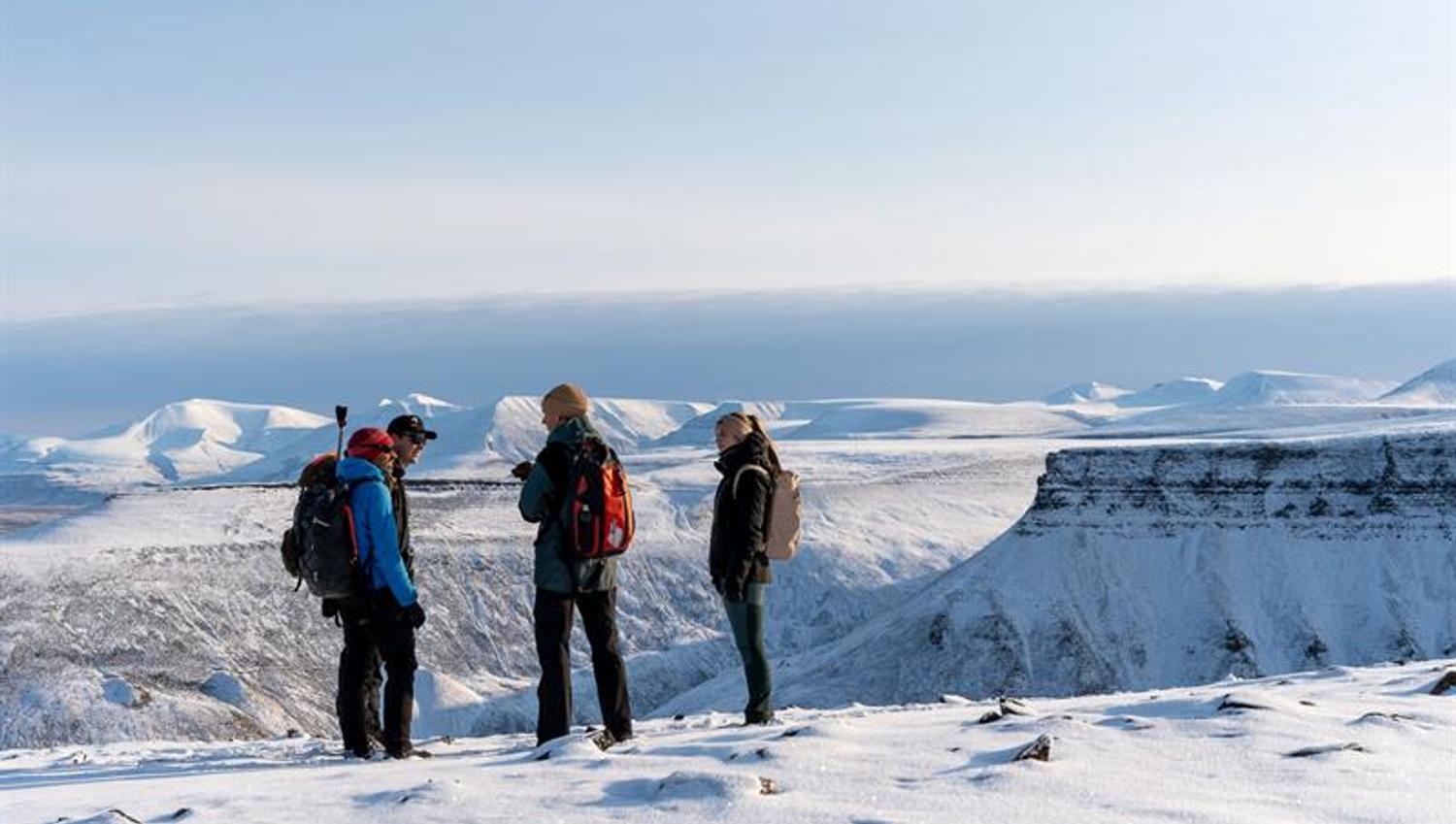 several people standing on top of snowcovered mountain. overlooking plateaus and other mountains in the background