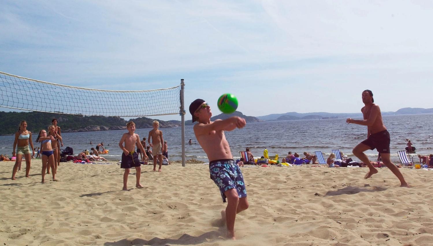 En gjeng som spiller strandvolleyball, der en fyr skal serve en grønn volleyball