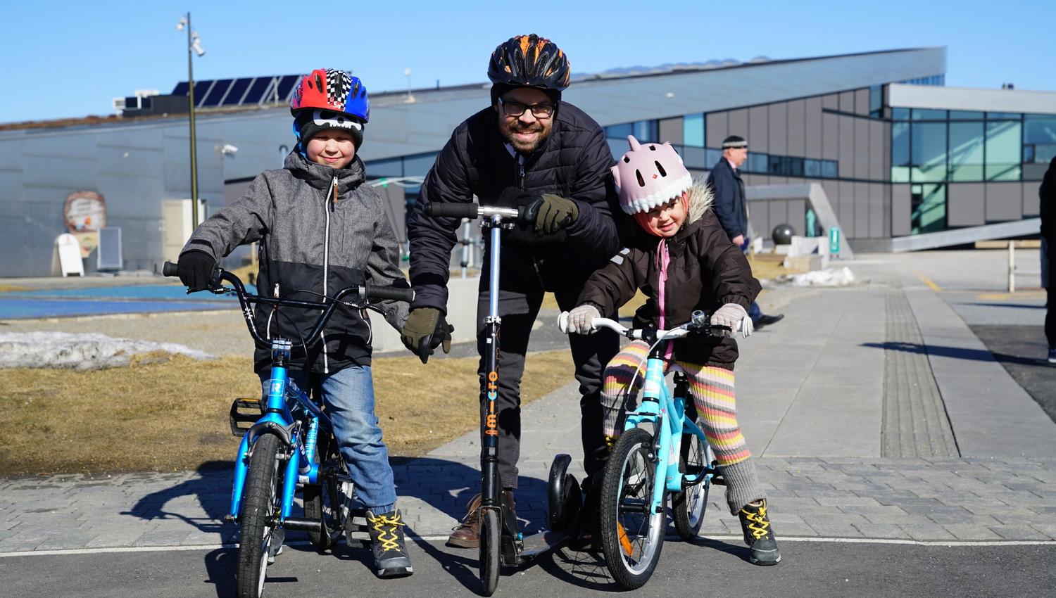A girl and a boy on a bike and a man on a scooter test out the activity park