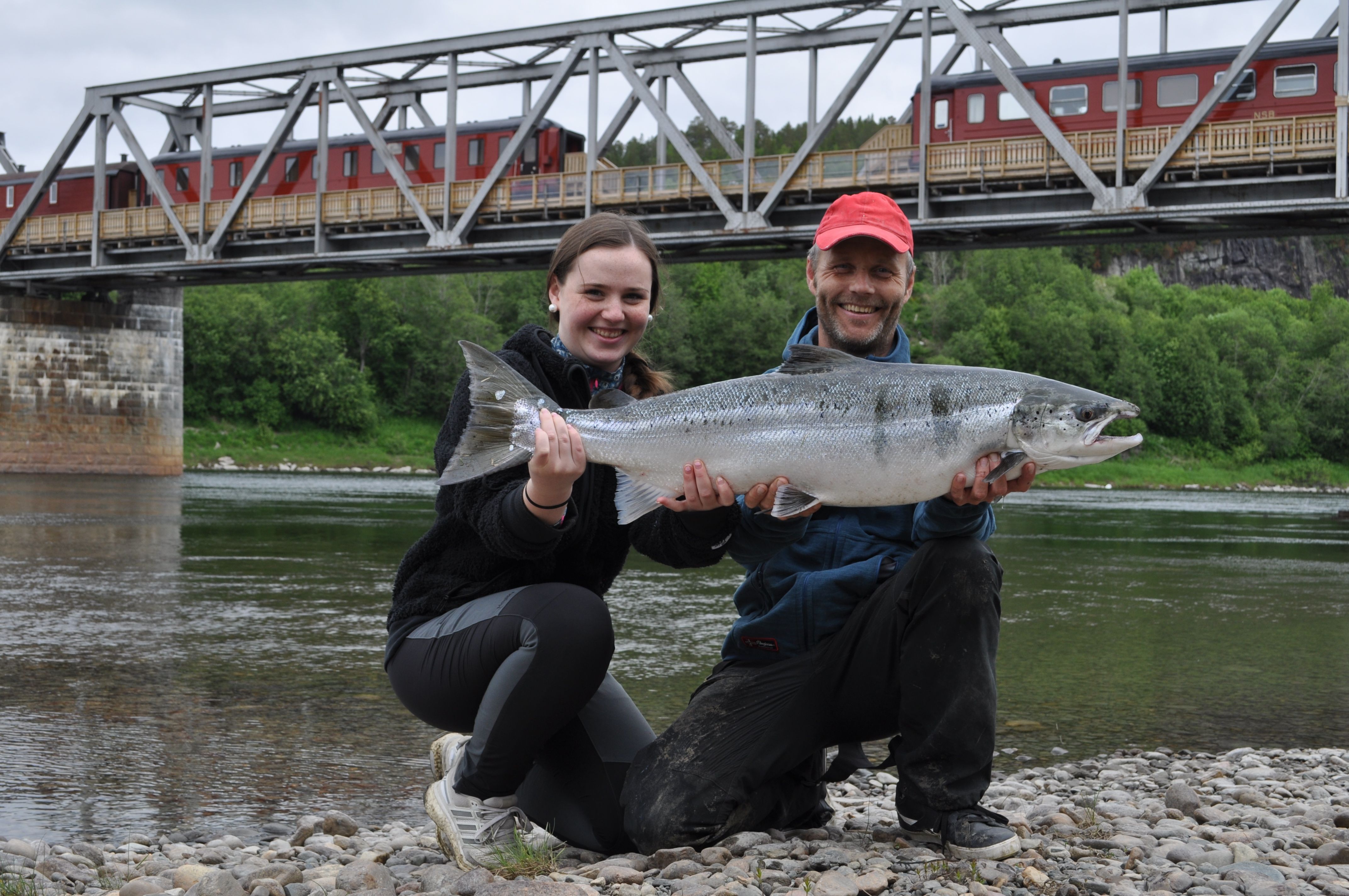 En mann og en dame holder opp en stor laks som de har fanget i Namsen, ved Namsen Salmon and Train Experience i Overhalla.
