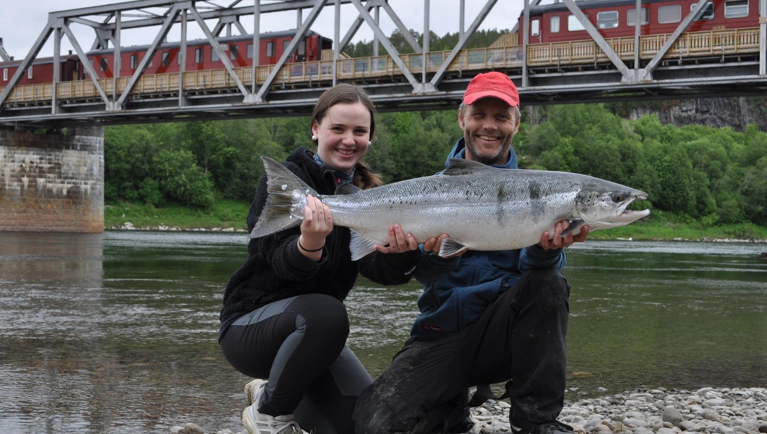 En mann og en dame holder opp en stor laks som de har fanget i Namsen, ved Namsen Salmon and Train Experience i Overhalla.