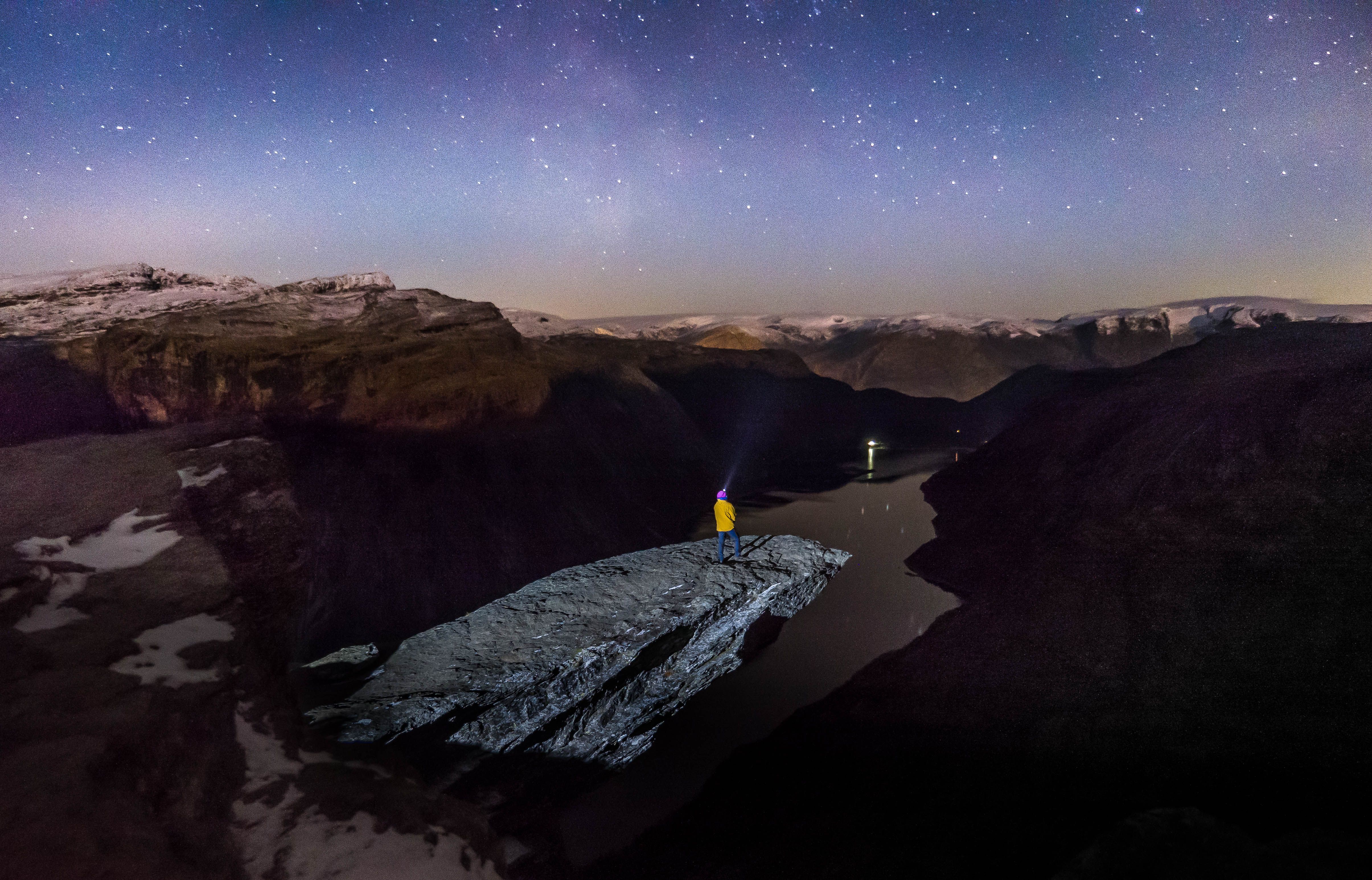 Mann står med hodelykt på Trolltunga under stjerneklar himmel.