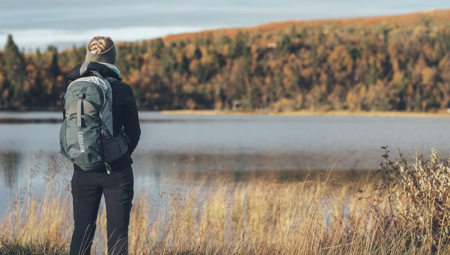Kvinne med tursekk ved fjellsjø