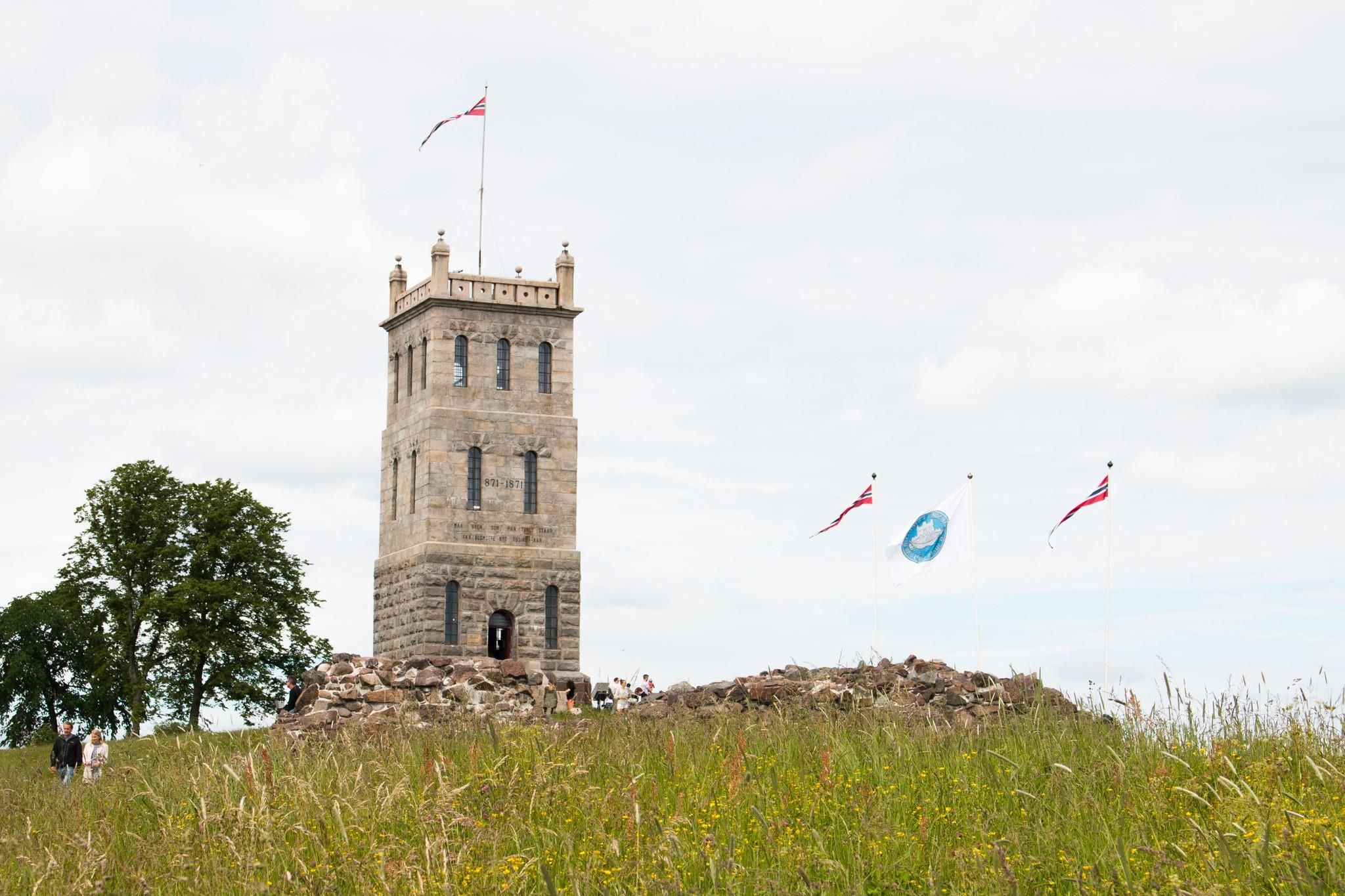 Slottsfjelltårnet med flagg på toppen, med gresslette i forgrunnen, og tre flagg på høyre side.