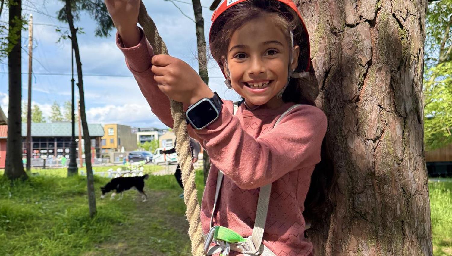 A child holding onto a rope, preparing to climb or swing in the obstacle course.