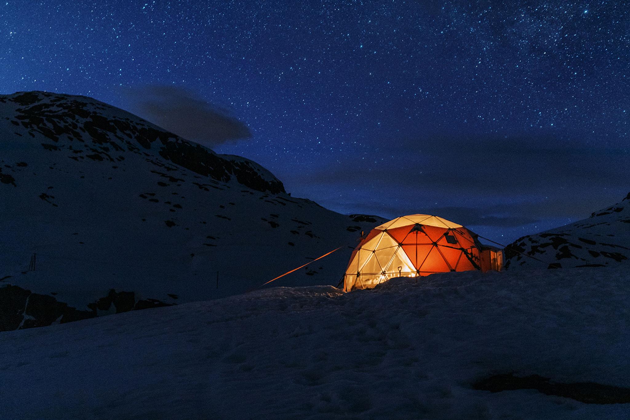 Illuminated geodome in a snowy mountain landscape under a starry winter sky near Trolltunga.