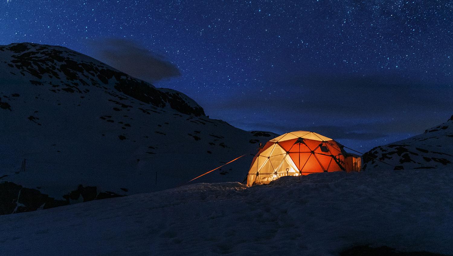 Opplyst geodome i snødekt fjellandskap under stjerneklar vinterhimmel ved Trolltunga.