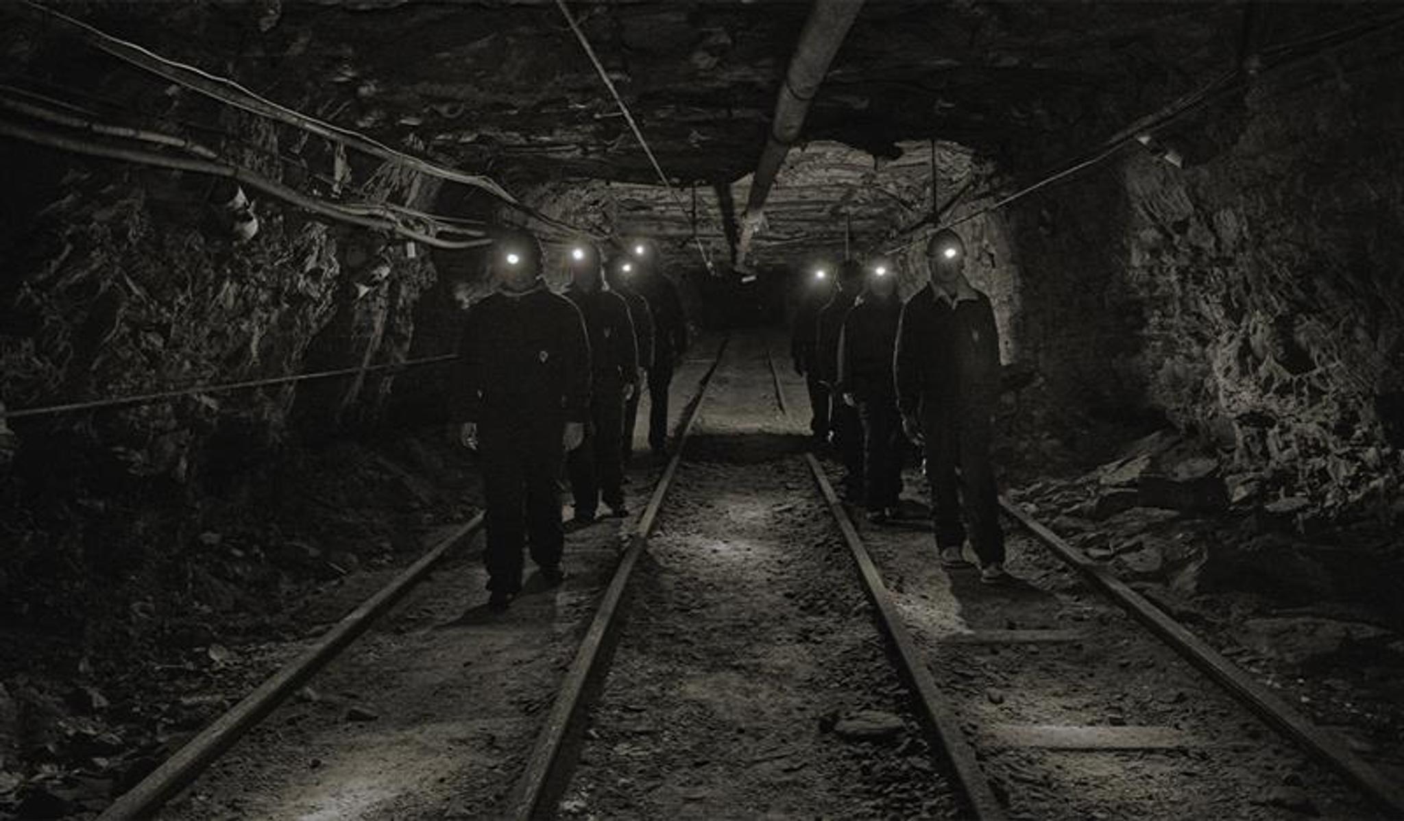 A group of guests with head lamps and helmets on, walking through a mine passage on a guided tour