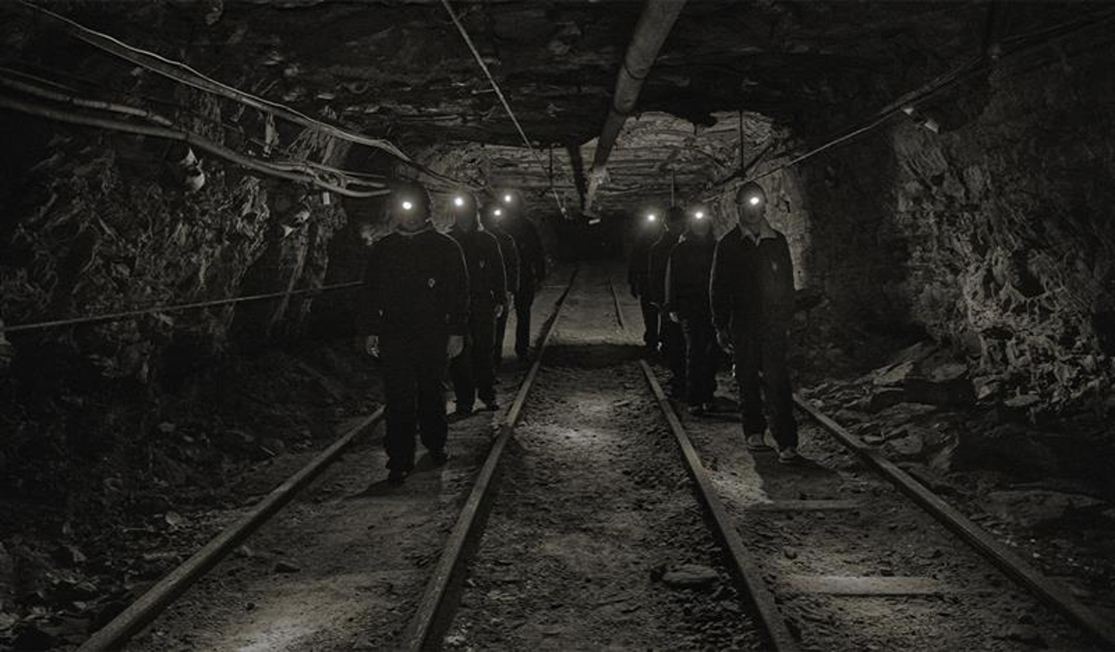 A group of guests with head lamps and helmets on, walking through a mine passage on a guided tour