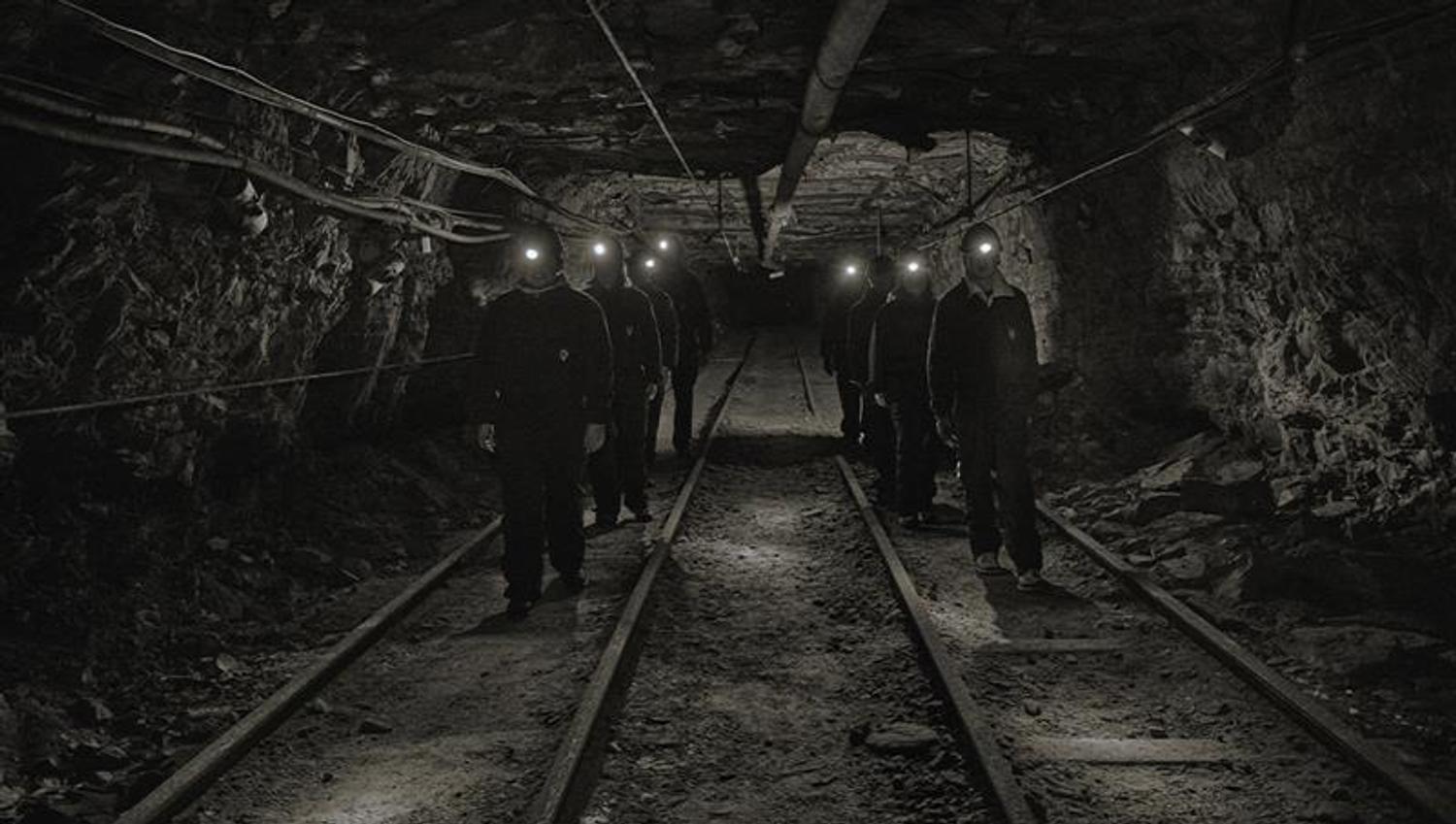 A group of guests with head lamps and helmets on, walking through a mine passage on a guided tour