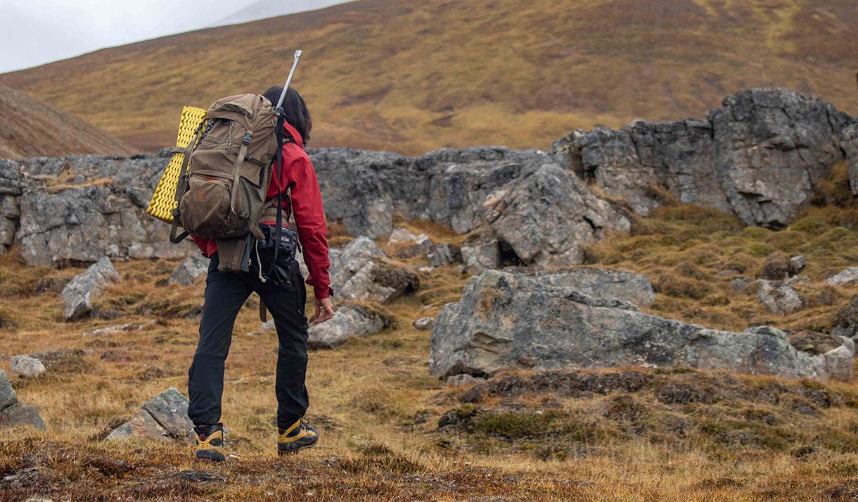 A guide with a backpack and rifle on their back hiking up a mountainside