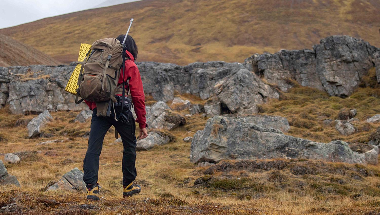 A guide with a backpack and rifle on their back hiking up a mountainside