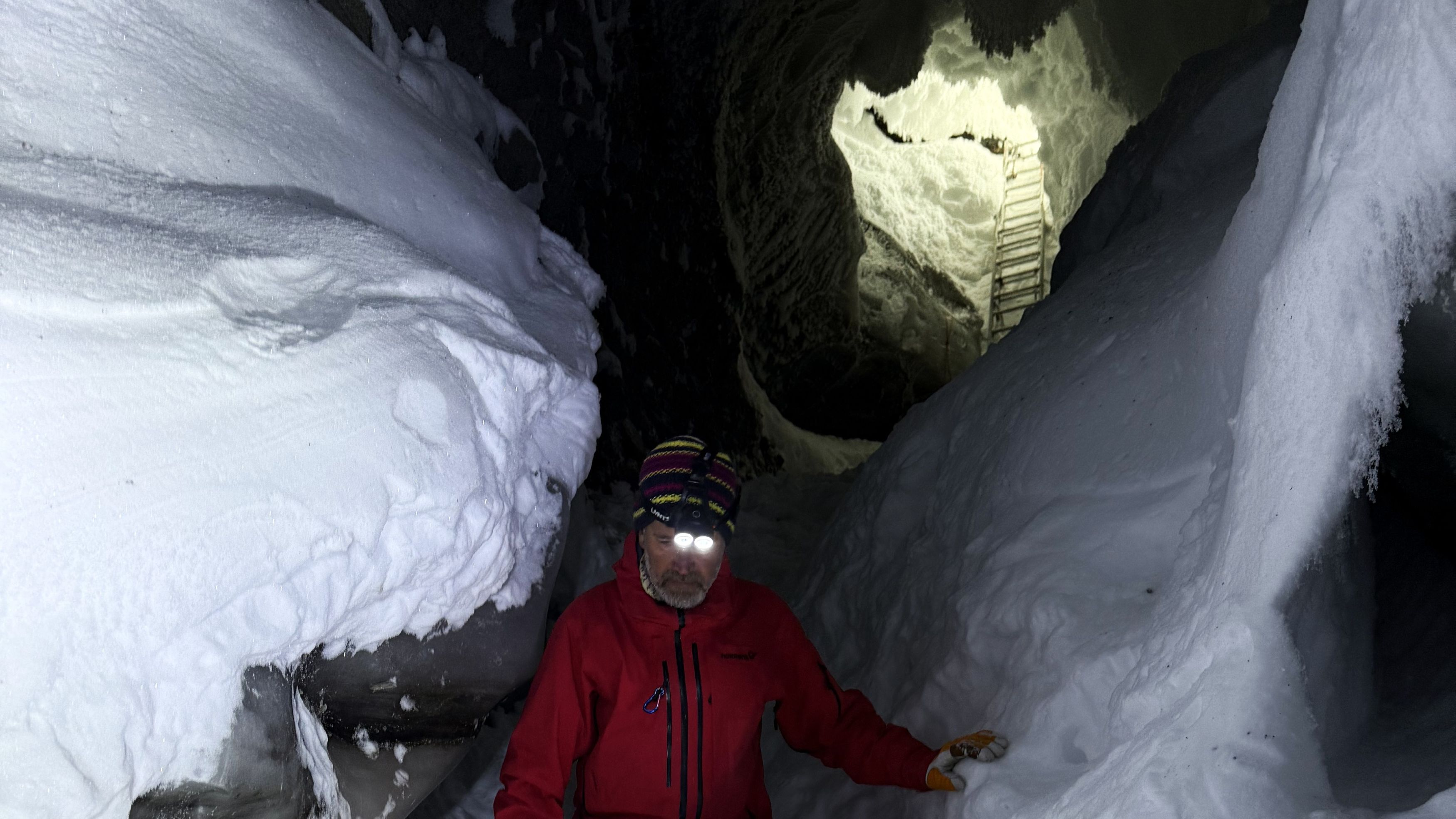 A person walking inside an ice cave. The entrence to the ice cave is visible in the background