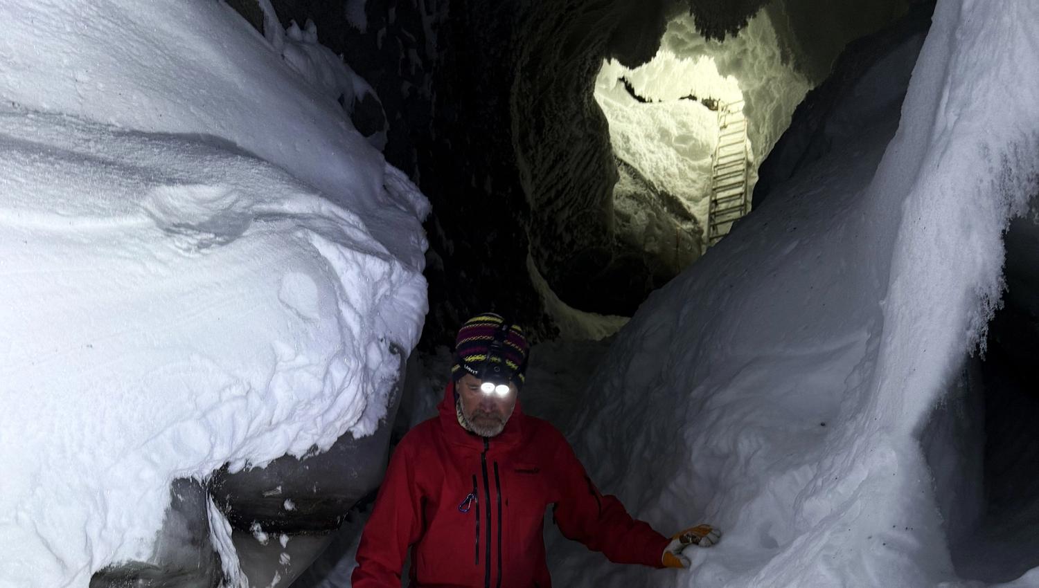 A person walking inside an ice cave. The entrence to the ice cave is visible in the background