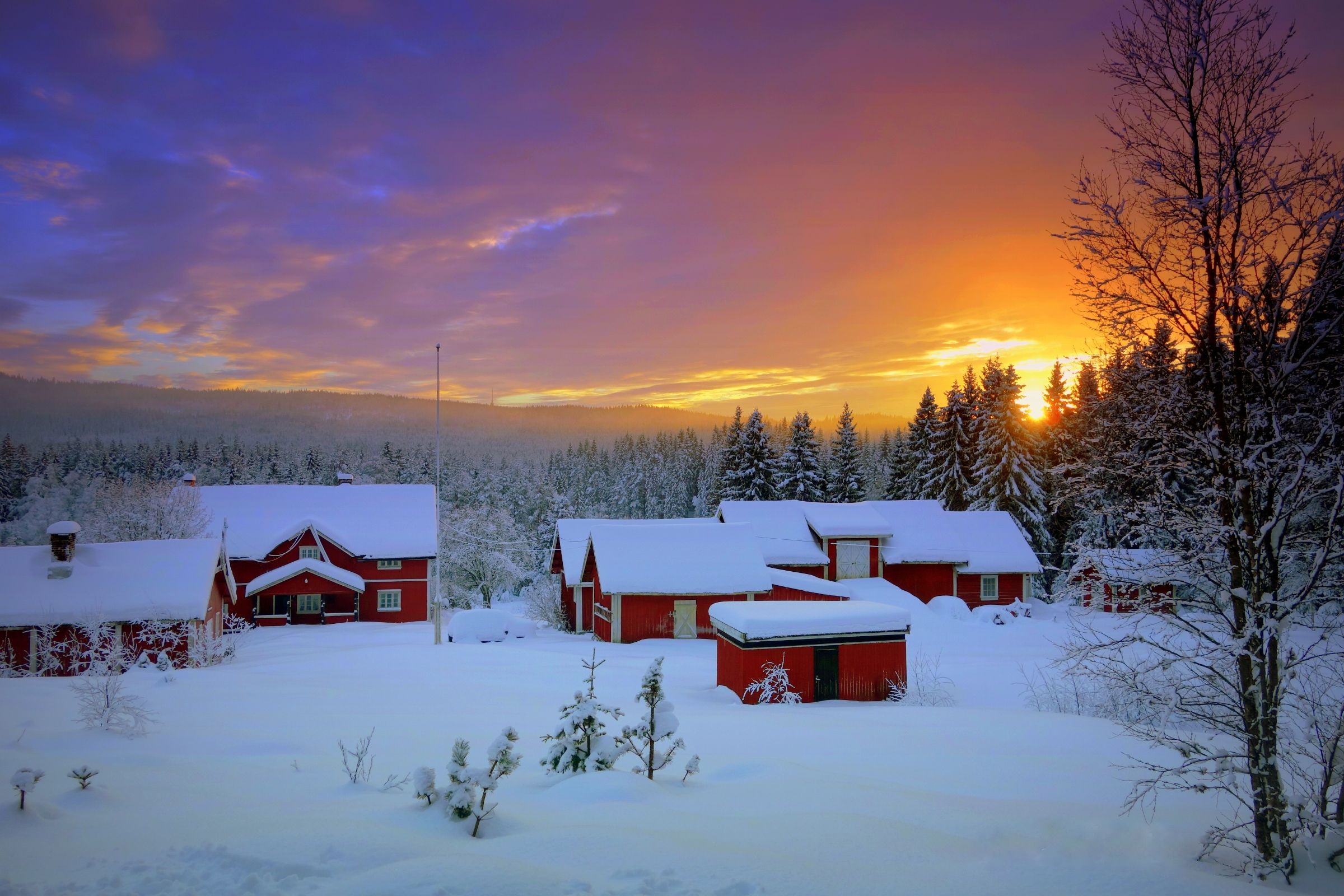 Snødekte trehytter med solnedgang i bakgrunnen.