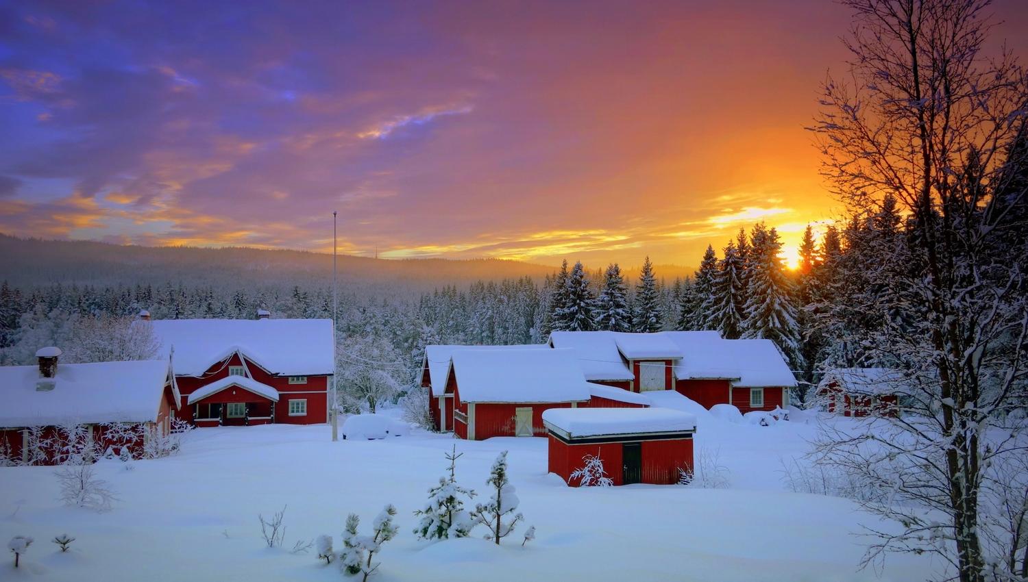 Snødekte trehytter med solnedgang i bakgrunnen.