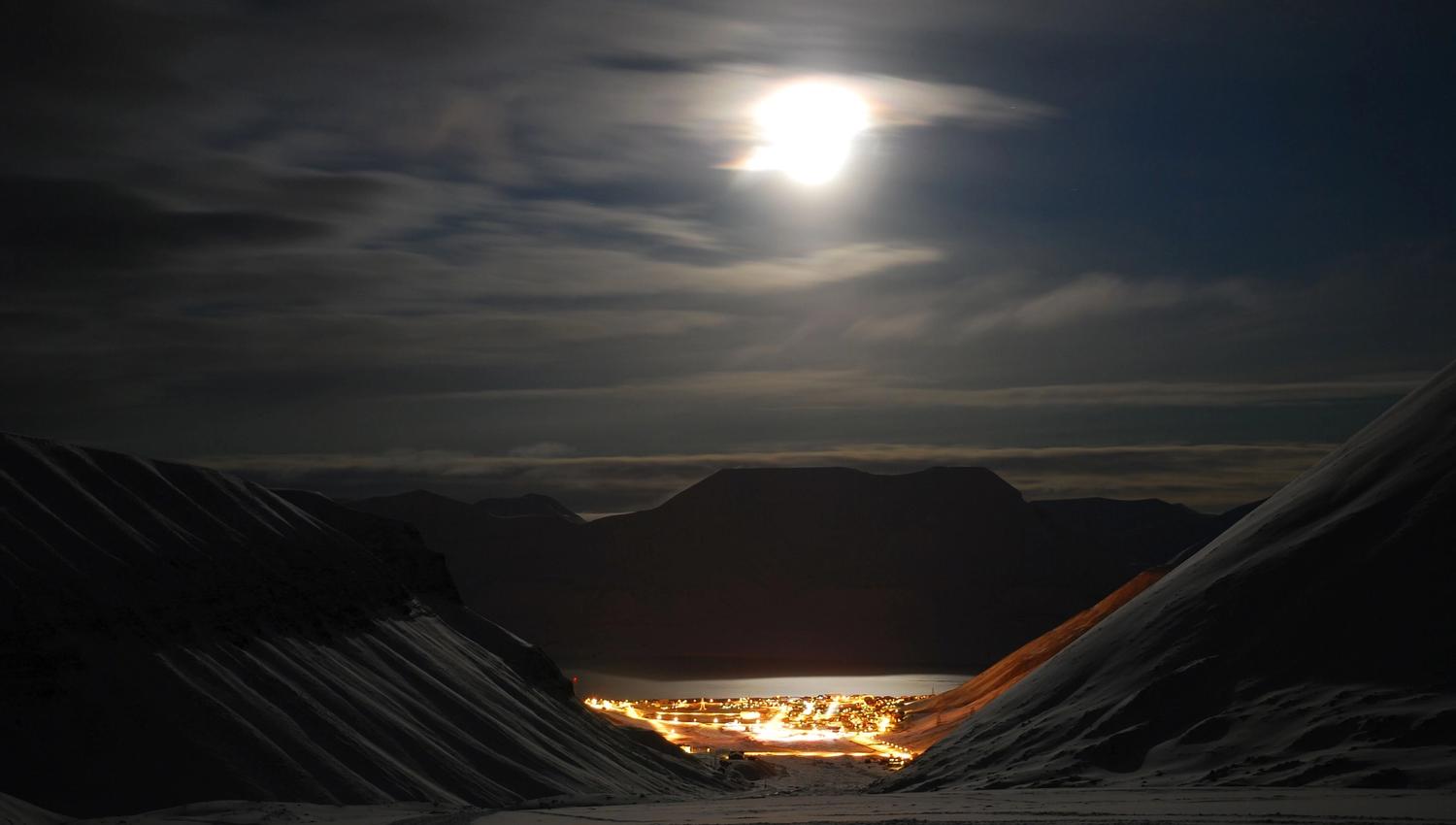 Longyearbyen at the end of the valley. The moonlight lights up the surrounding mountains.