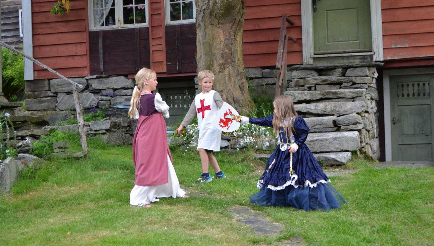 Tre ungar kledd i middelalderkostymer leikar i hagen