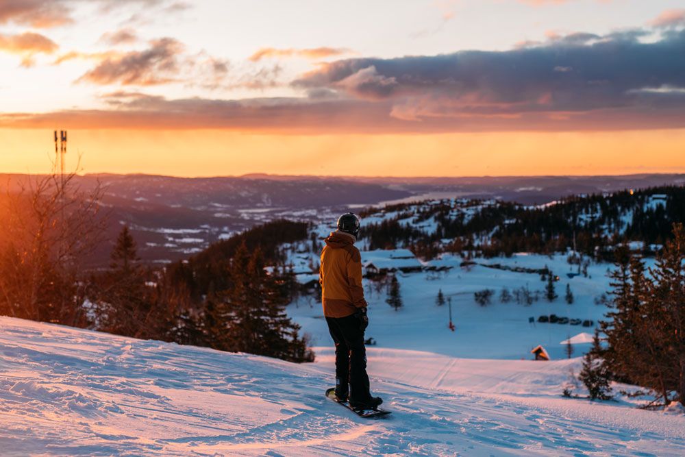 gutt på snowboard på toppen av alpinbakken på Lifjell skisenter i solnedgang