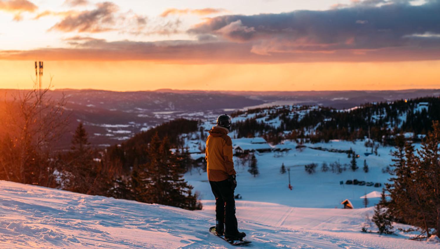 gutt på snowboard på toppen av alpinbakken på Lifjell skisenter i solnedgang