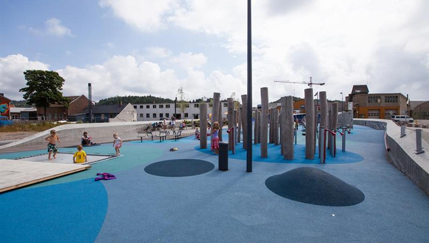 Buen Playground, blue in different shades on the ground with many different play equipment. Trampoline, swing, climbing wall, balance line.
