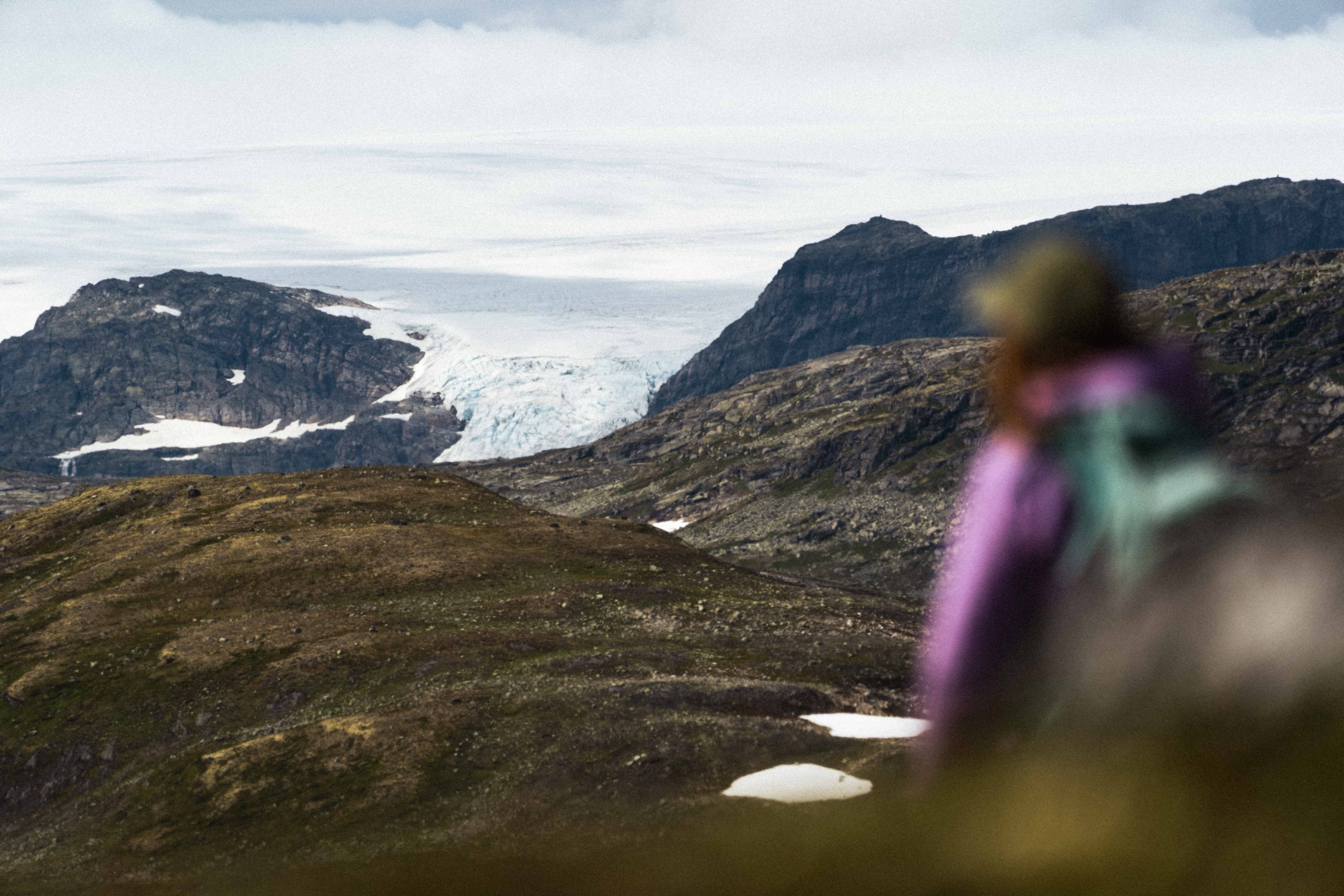 A woman in a pink jacket with the Hardangerjøkulen glacier in the background.