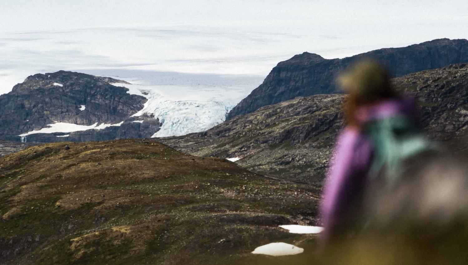 A woman in a pink jacket with the Hardangerjøkulen glacier in the background.
