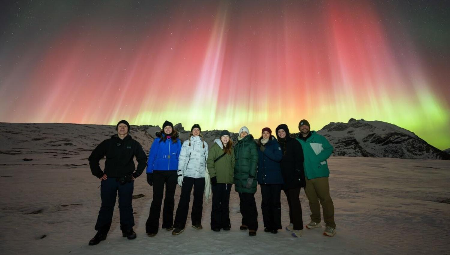 En gruppe med gjester poserer foran rødt og grønt nordlys