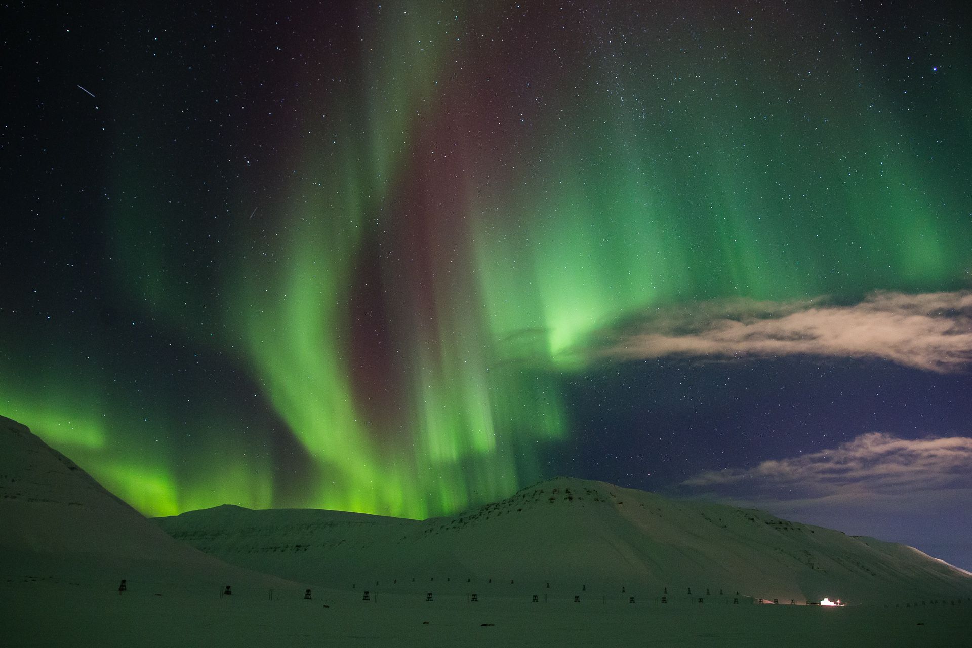 Et fjellandskap i forgrunnen med nordlys på himmelen i bakgrunnen