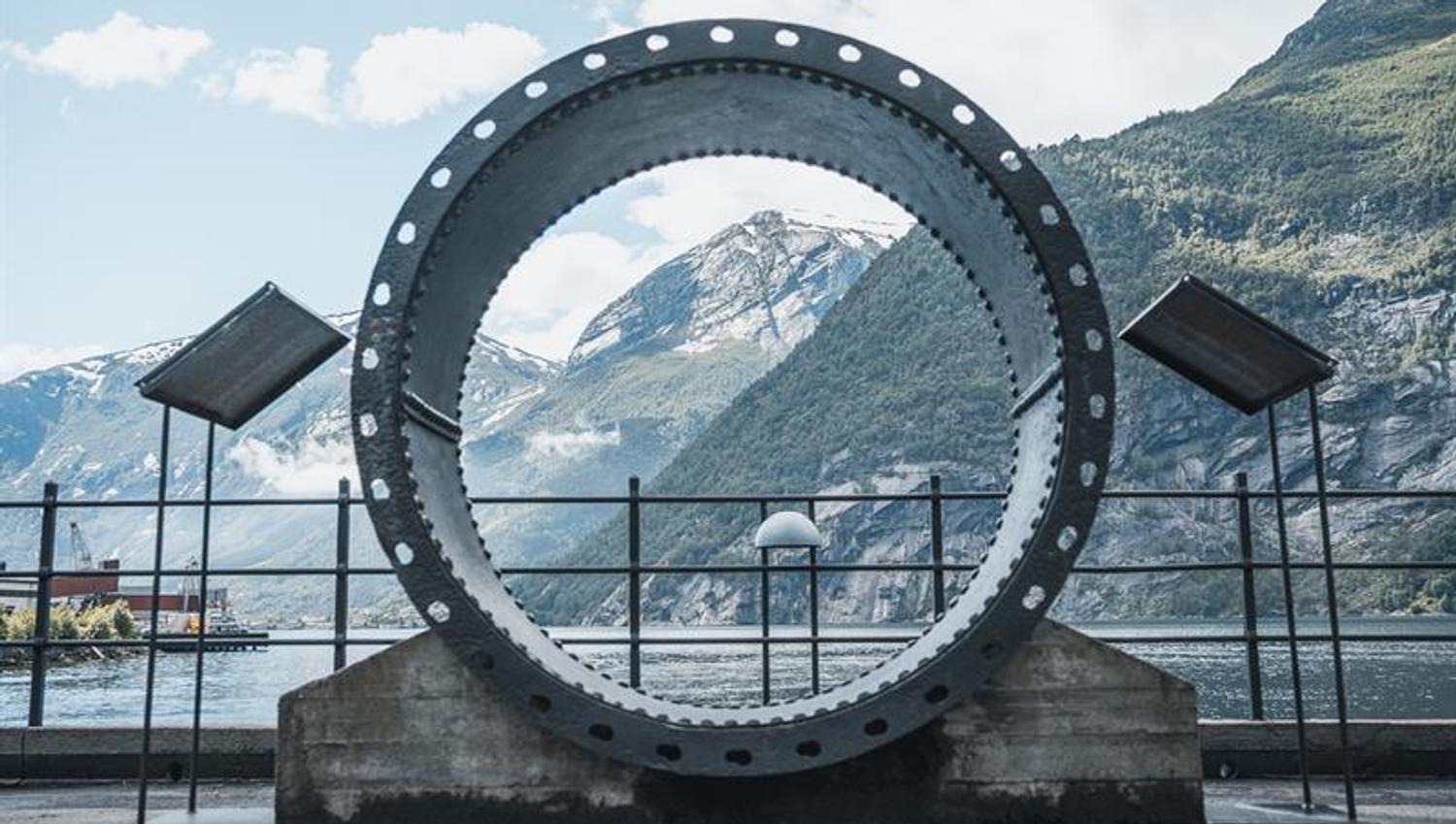 Utandørs utstilling ved Kraftmuseet med ein stor turbinring og utsikt over fjorden og fjella i Hardanger.