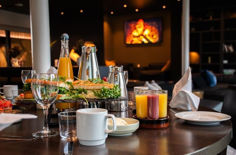 Bord med frokostservering, juice, kaffe og glass, i en lun og stemningsfull lounge.